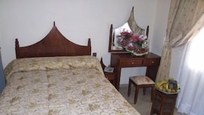 Un dormitorio con una cama, una mesita de noche de madera, un escritorio con un espejo y una silla.