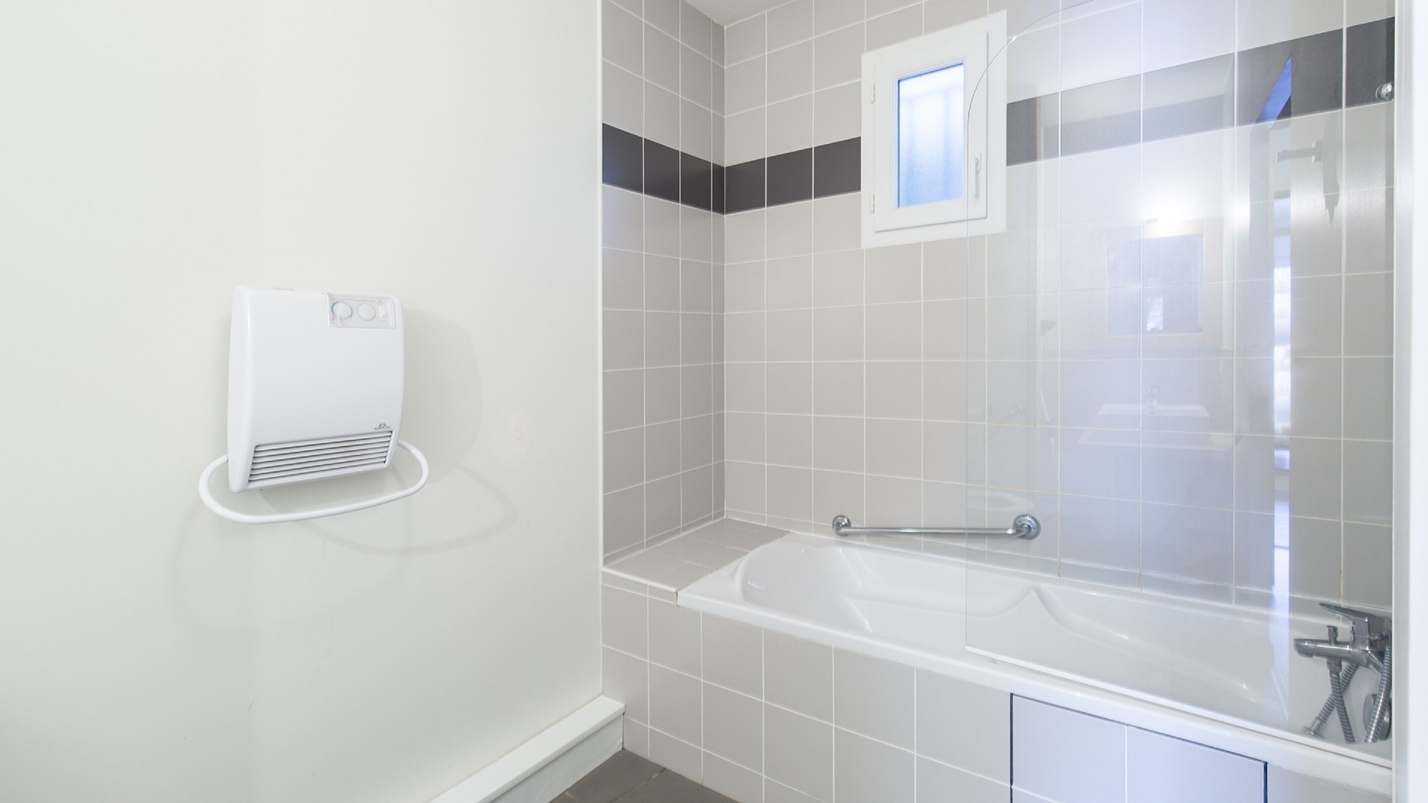 Une salle de bain avec une baignoire blanche, un porte-serviettes et un radiateur fixé au mur.