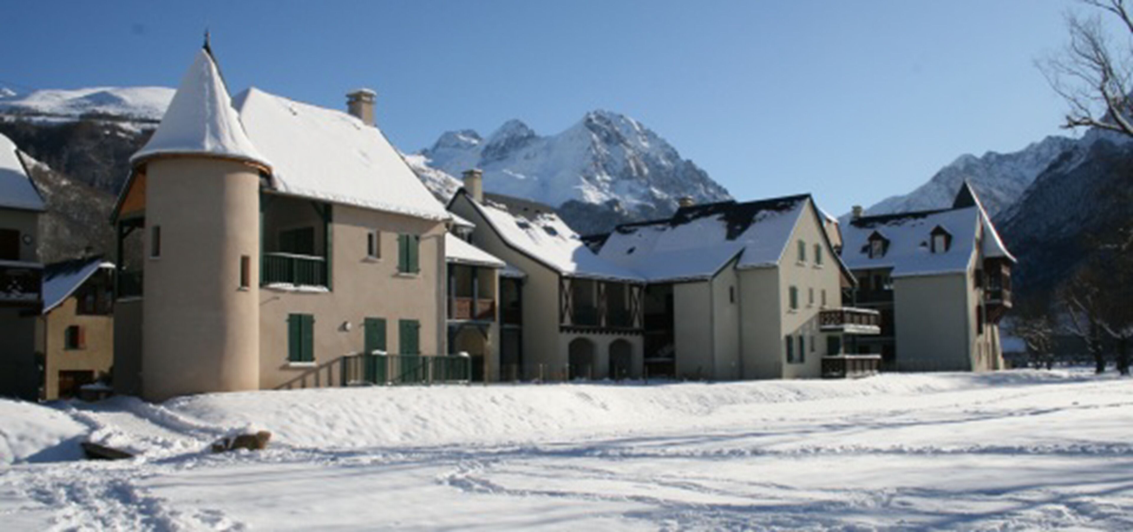 Un edificio cubierto de nieve con numerosas ventanas y techo nevado, rodeado de montañas.