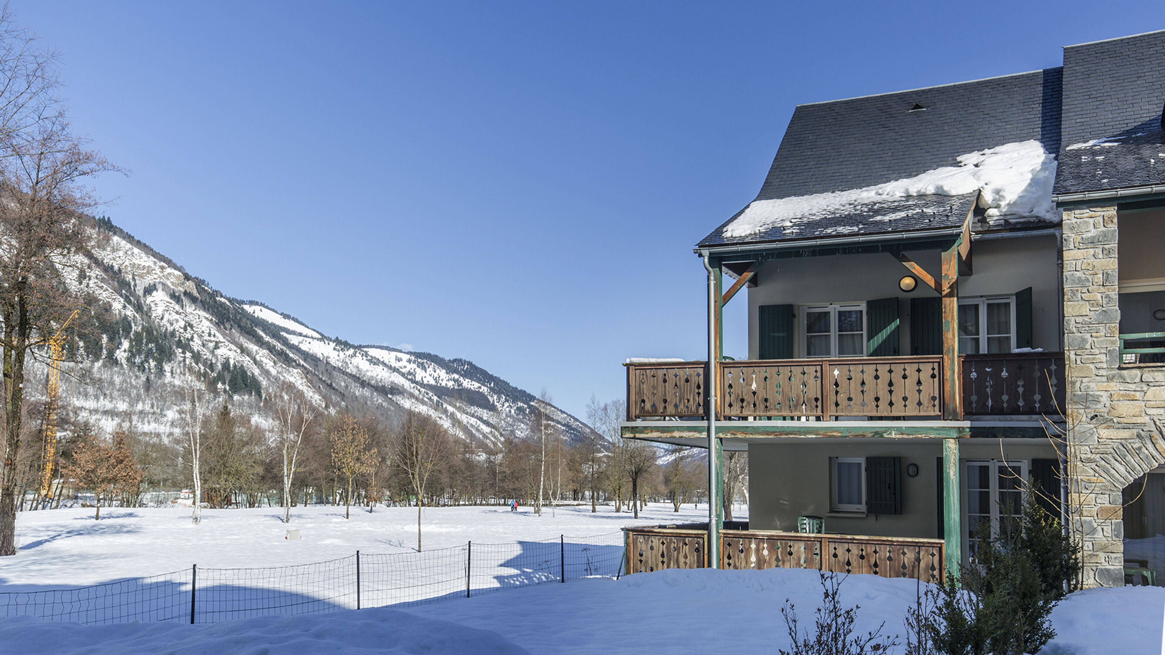 Un bâtiment à deux étages doté d’un balcon, entouré d’un paysage enneigé et avec des montagnes en arrière-plan.