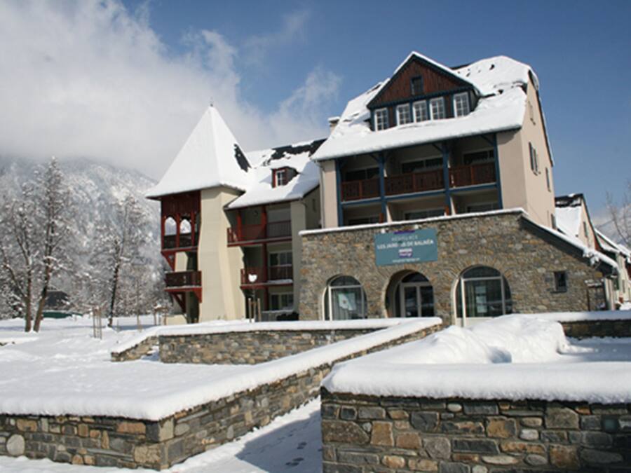 A multi-story building with stone walls and a snow-covered roof, surrounded by snow-covered trees.