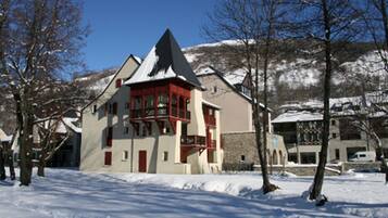 Un edificio cubierto de nieve con un balcón rojo, rodeado de árboles y una montaña al fondo.