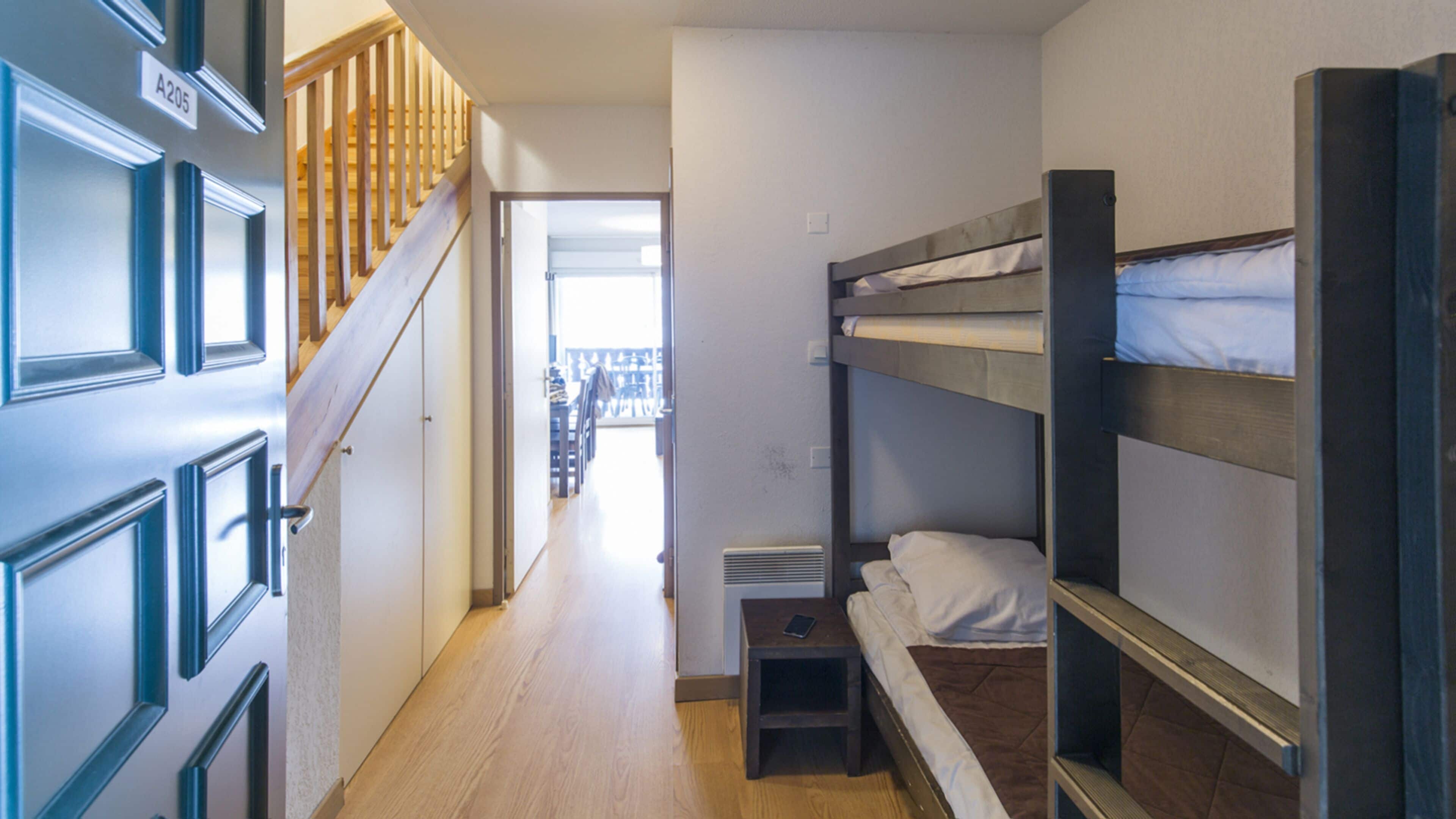 A dormitory room with bunk beds, a wooden staircase, and a door labeled A205.