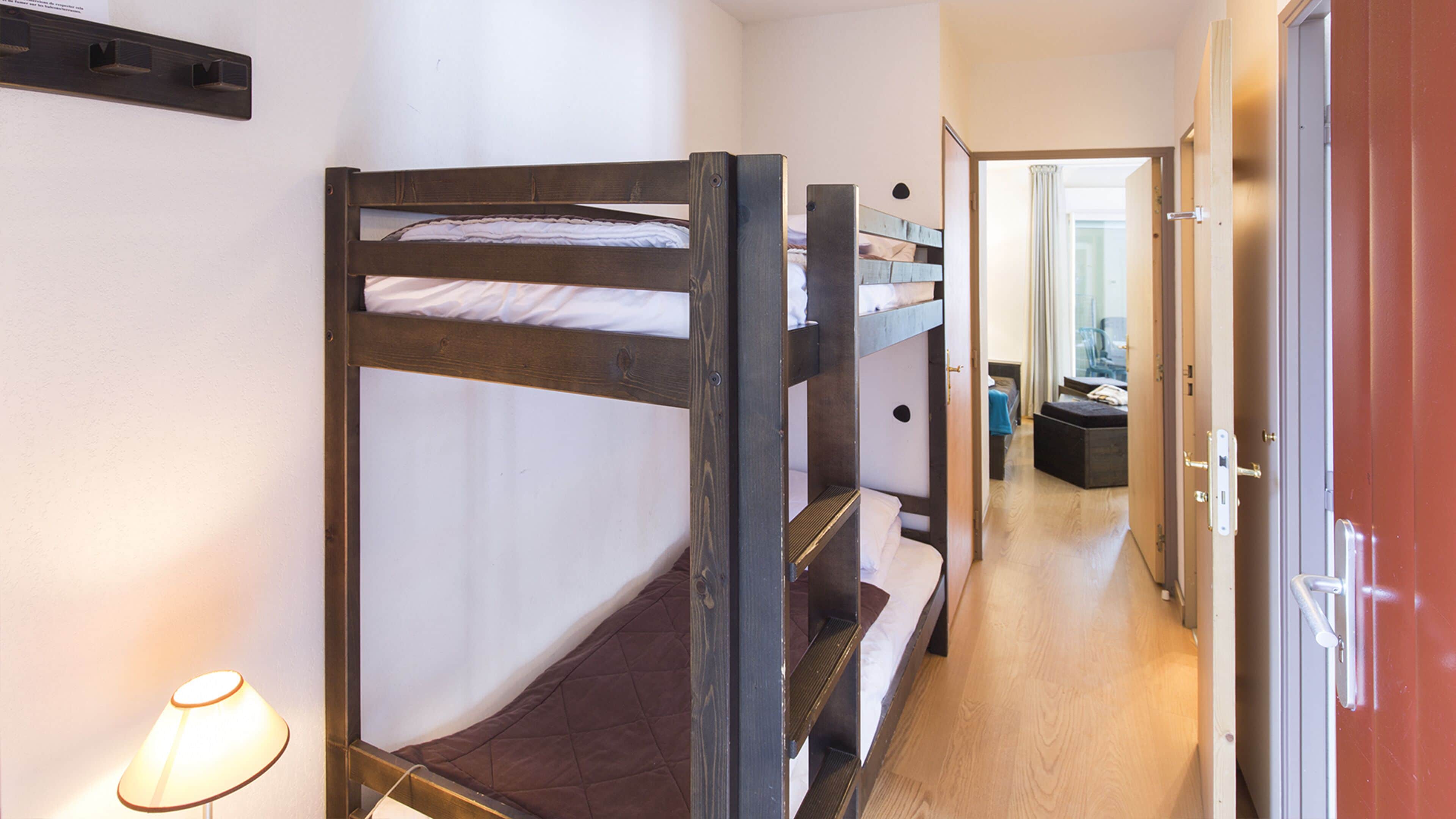 A bunk bed room with a wooden frame, a bedside table, and a lamp.