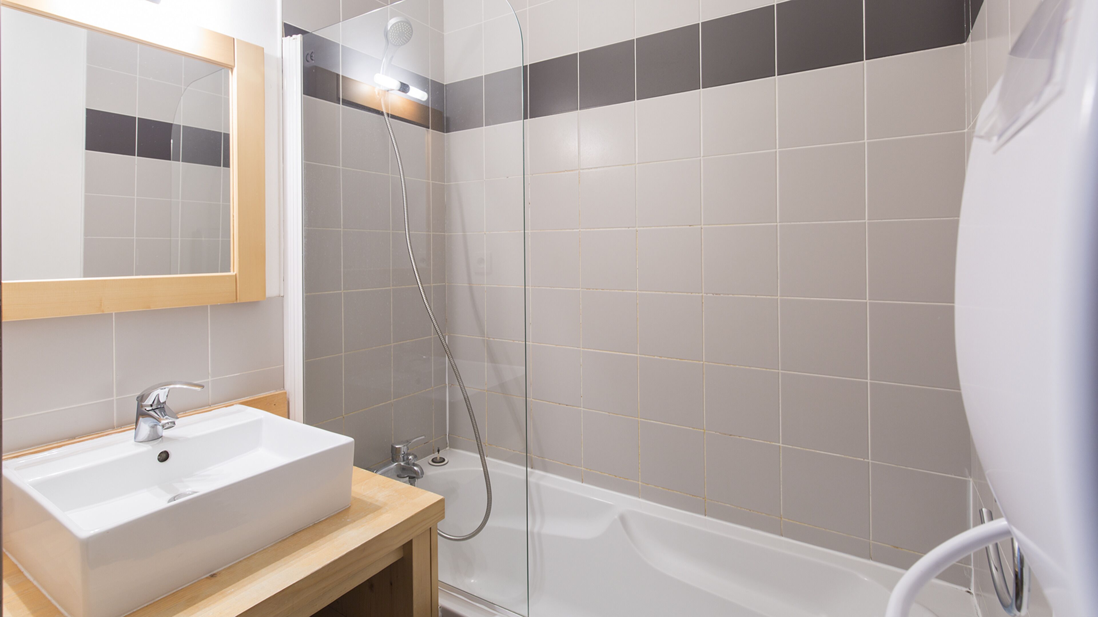 Un baño con lavamanos blanco, espejo y zona de ducha.