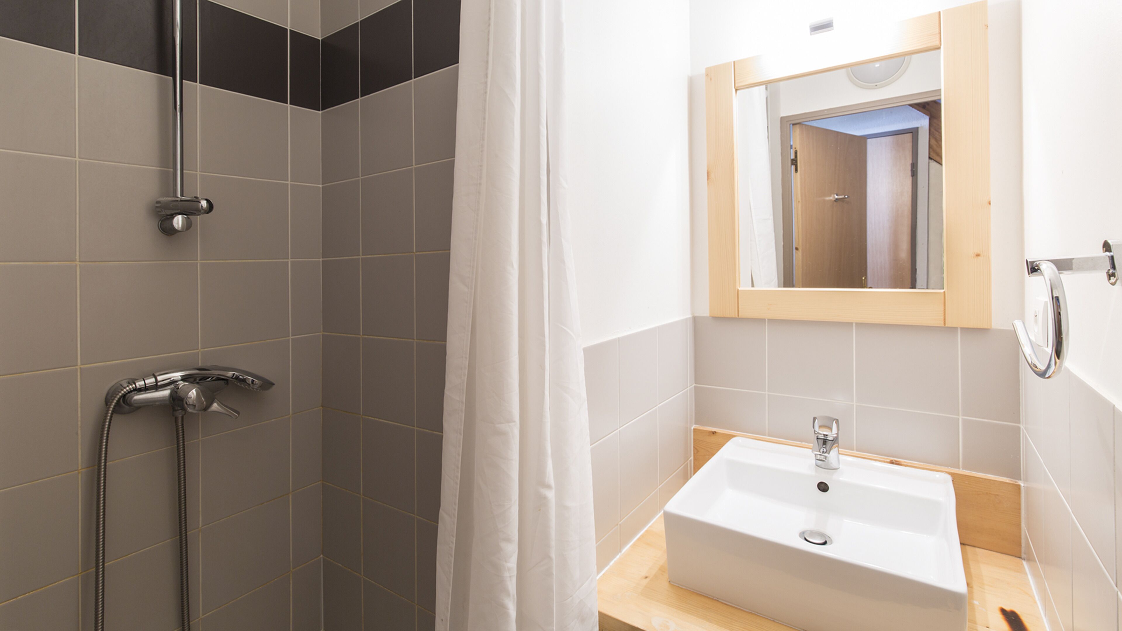 Een badkamer met een douche, wastafel en spiegel.