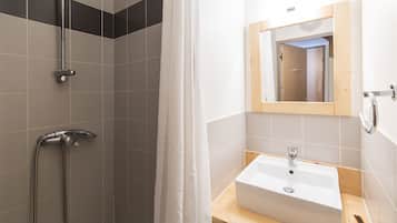 Een badkamer met een douche, wastafel en spiegel.