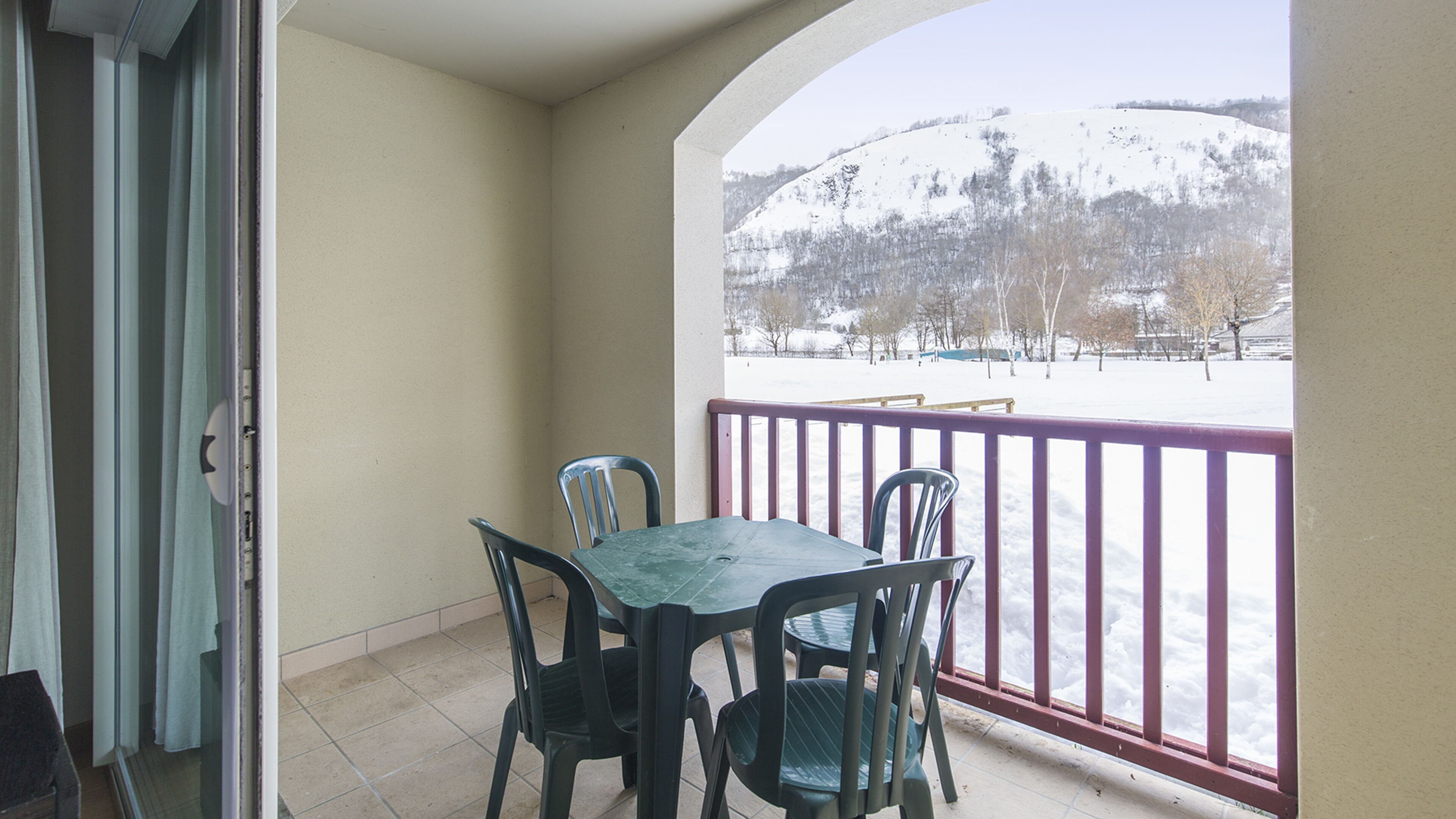 Un balcon avec une table et des chaises, donnant sur un paysage enneigé avec des arbres et une colline.
