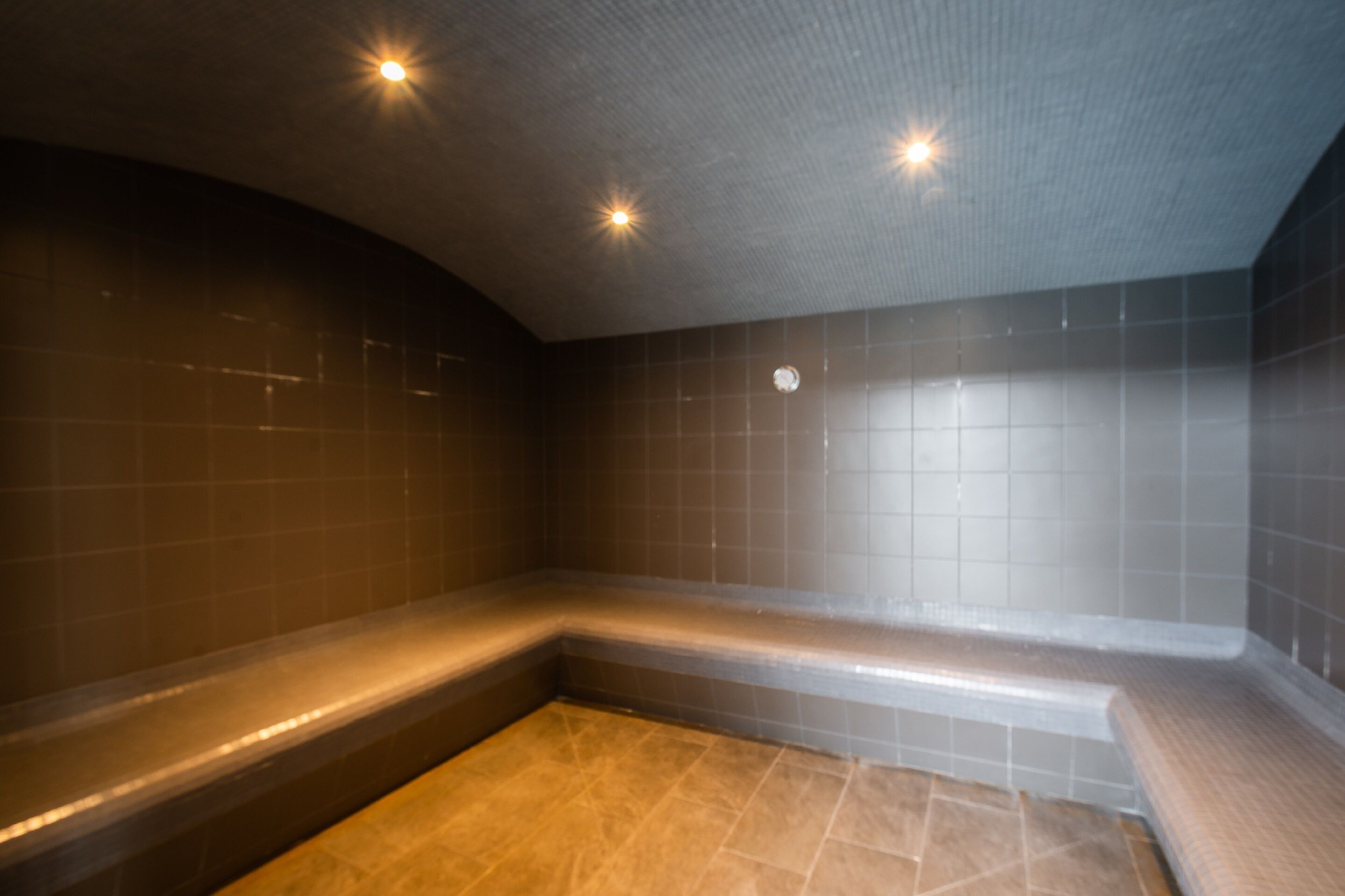 A modern bathroom with a curved bench, tiled walls, and recessed lighting.