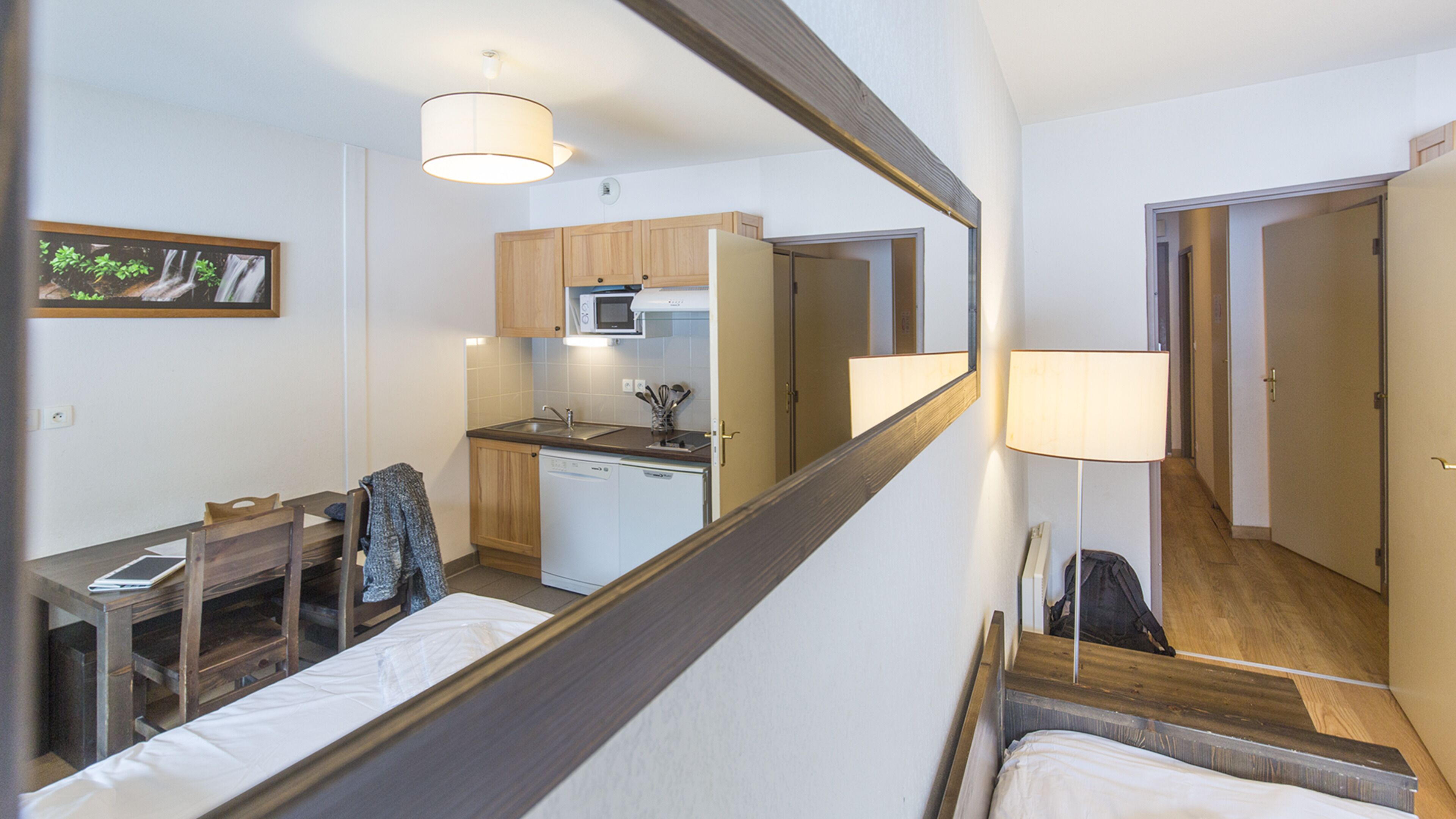 Une chambre d’hôtel compacte dotée d’une kitchenette, d’un coin repas et d’un grand miroir.