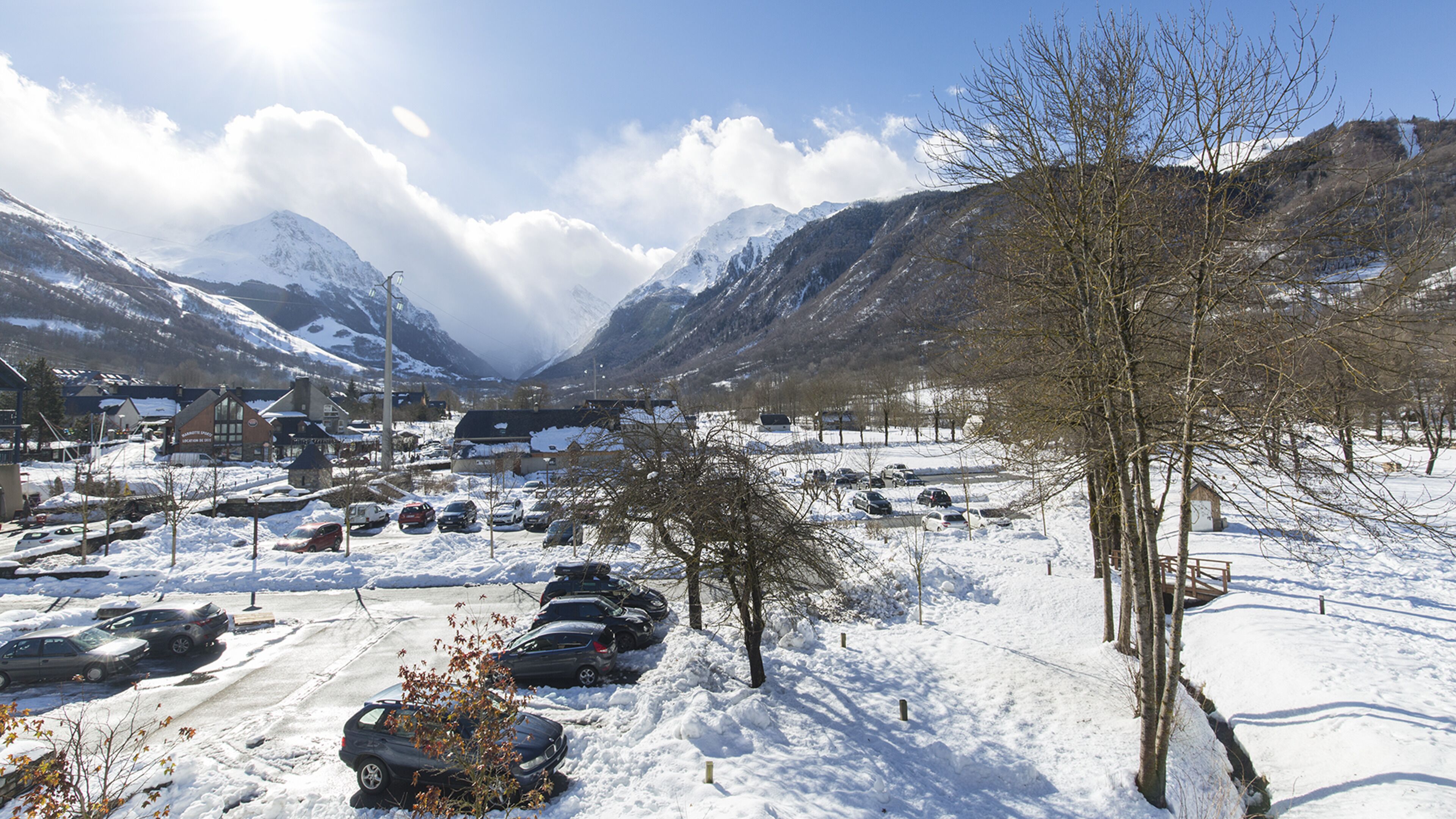 Uma aldeia montanhosa coberta de neve, com carros estacionados e edifícios.