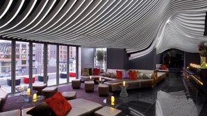 Un salón moderno con lámparas de techo curvas, asientos cómodos y amplios ventanales con vistas a la ciudad.