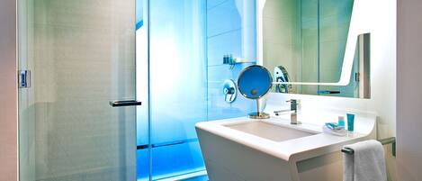 A modern bathroom with a glass shower enclosure, a white sink with a mirror, and a towel hanging on the wall.