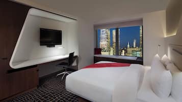 Una habitación de hotel moderna con cama, escritorio, silla, televisor y ventana con vista a la ciudad.