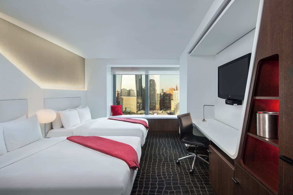A hotel room with two beds, a TV, a desk, and a window with a city view.