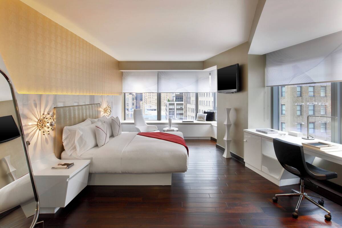 A modern hotel room with a large bed, a desk, a chair, and a TV.