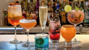 A variety of colorful cocktails on a bar counter with a backdrop of various liquor bottles.