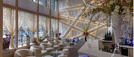 Eine moderne Bar mit Sitzgelegenheiten, einer großen Blumenvase und Blick auf die Straße durch große Fenster.