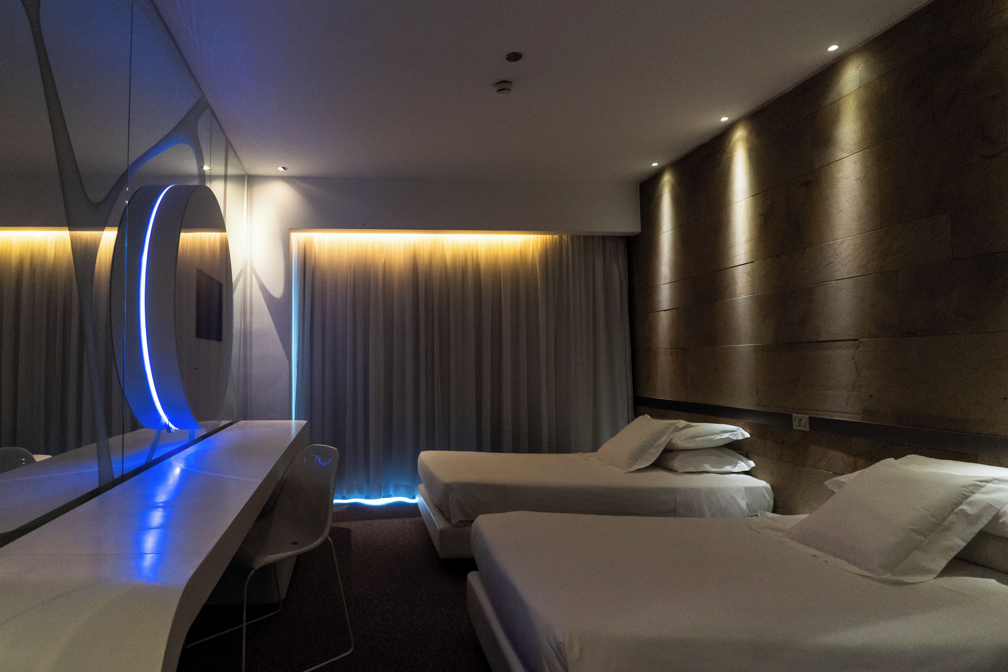 Ein modernes Hotelzimmer mit einem Bett, Nachttischen, einem Schreibtisch und einem großen Spiegel.