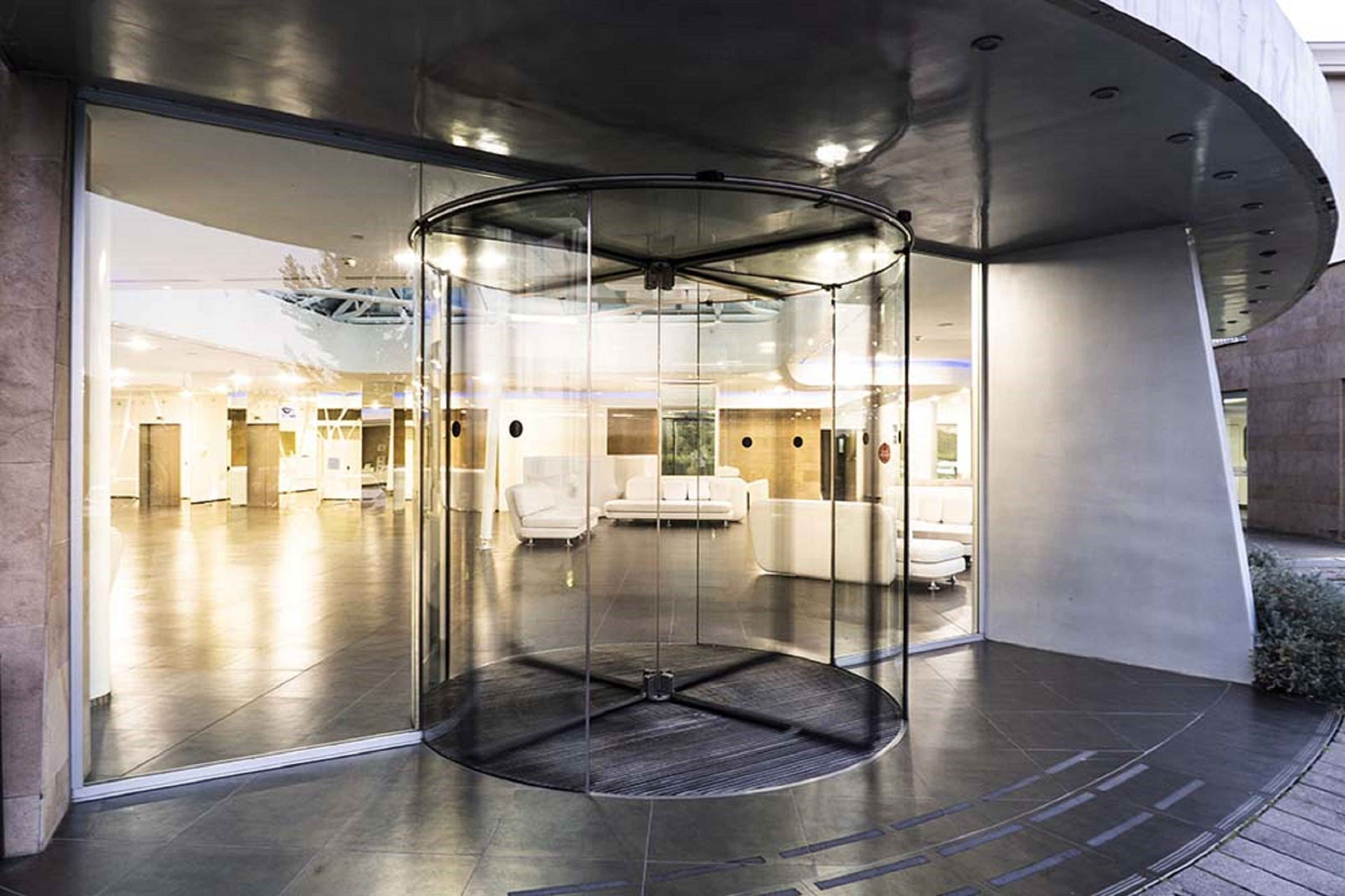 Un lobby moderno con puerta giratoria de vidrio, zona de estar con sofás blancos y un interior espacioso.