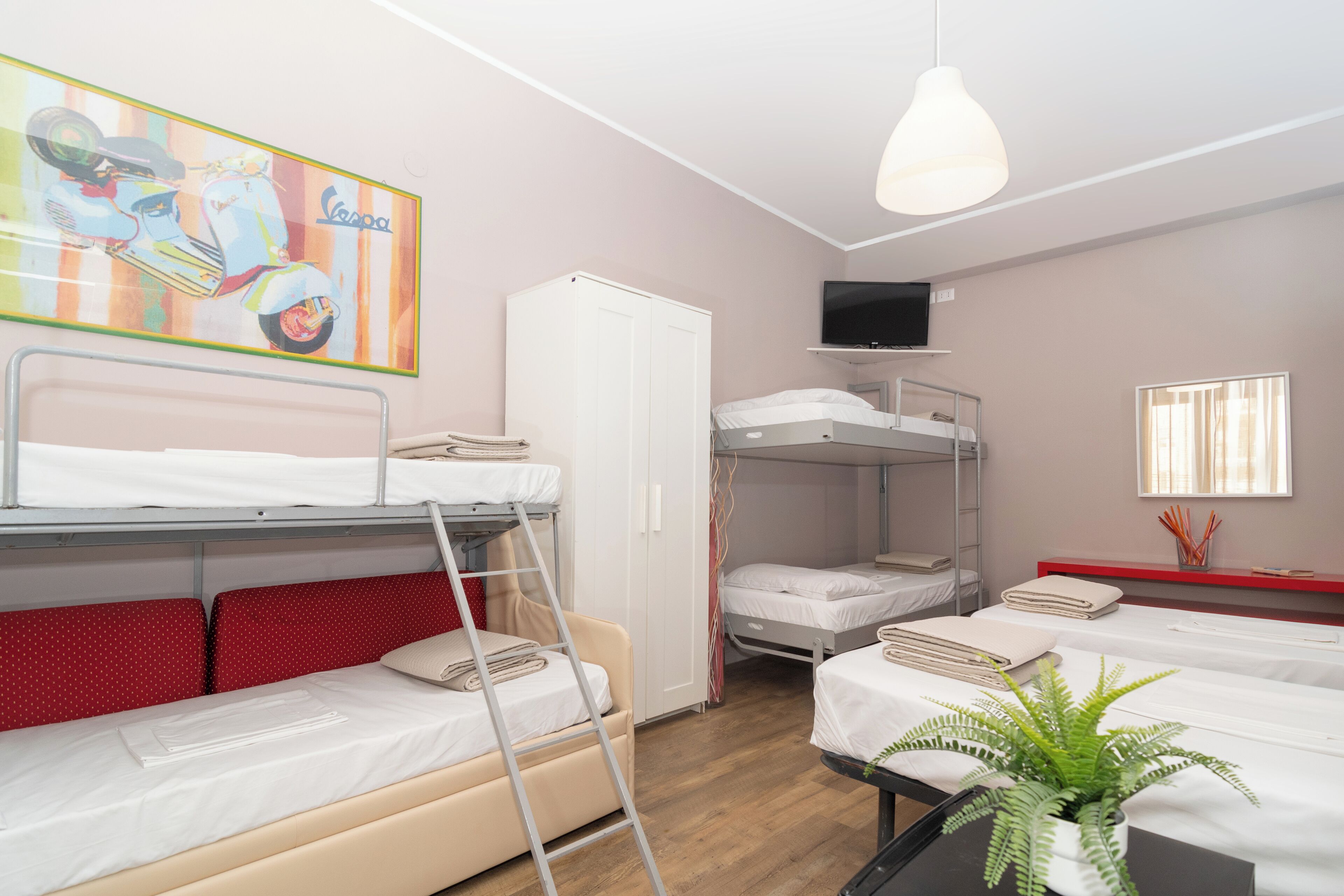 Un dormitorio con literas, televisión, armario y una planta en maceta.