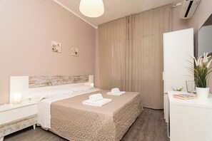 Un cuarto de hotel ordenado con cama, mesitas de noche, un escritorio y una planta en maceta.
