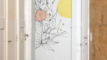Um corredor com piso de madeira, paredes brancas e porta com um mural floral.