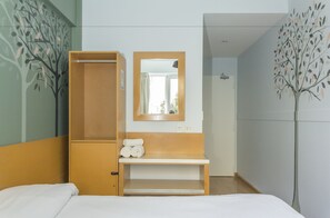 A hotel room with a bed, a wooden wardrobe, a mirror, and a wall-mounted shelf with towels. - Circus Hotel & Hostel (Buenos Aires)