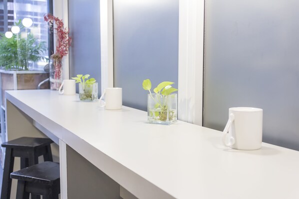 A white counter with three glass vases containing plants, a white mug, and a black stool. - Circus Hotel & Hostel (Buenos Aires)