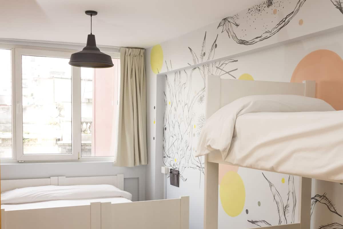 Quarto com beliche, escrivaninha e janela com cortinas.