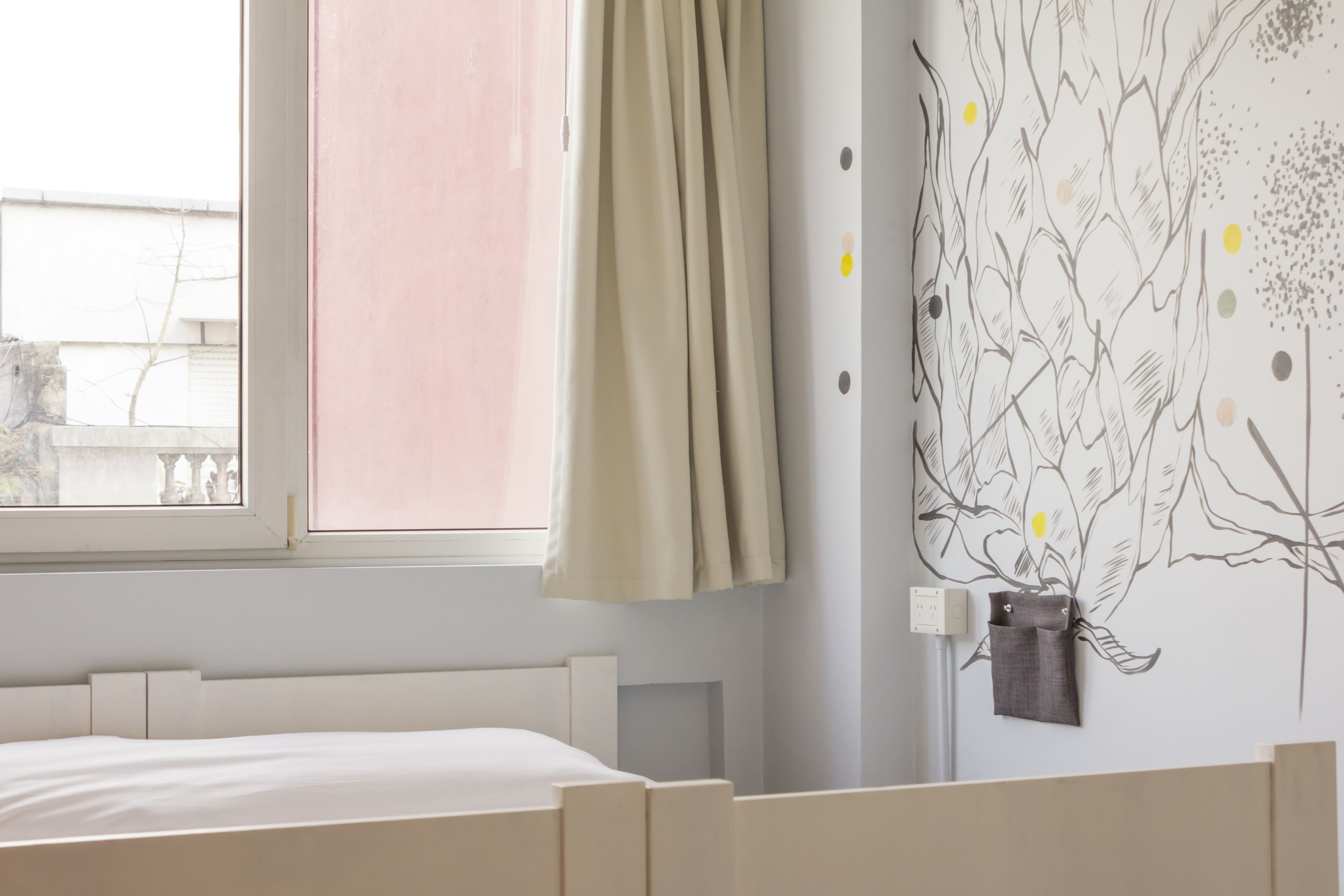 A bedroom with a bed, a window with a curtain, and a wall with a tree decal.