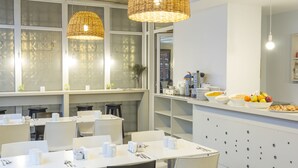 A modern dining area with white tables and chairs, a buffet counter with fruits and snacks, and wicker pendant lights. - Circus Hotel & Hostel (Buenos Aires)