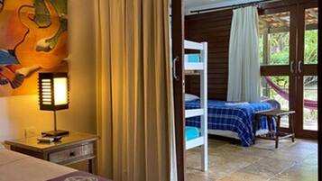 Habitación de hotel con cama, mesita de noche, un cuadro y vista a un balcón con hamaca.