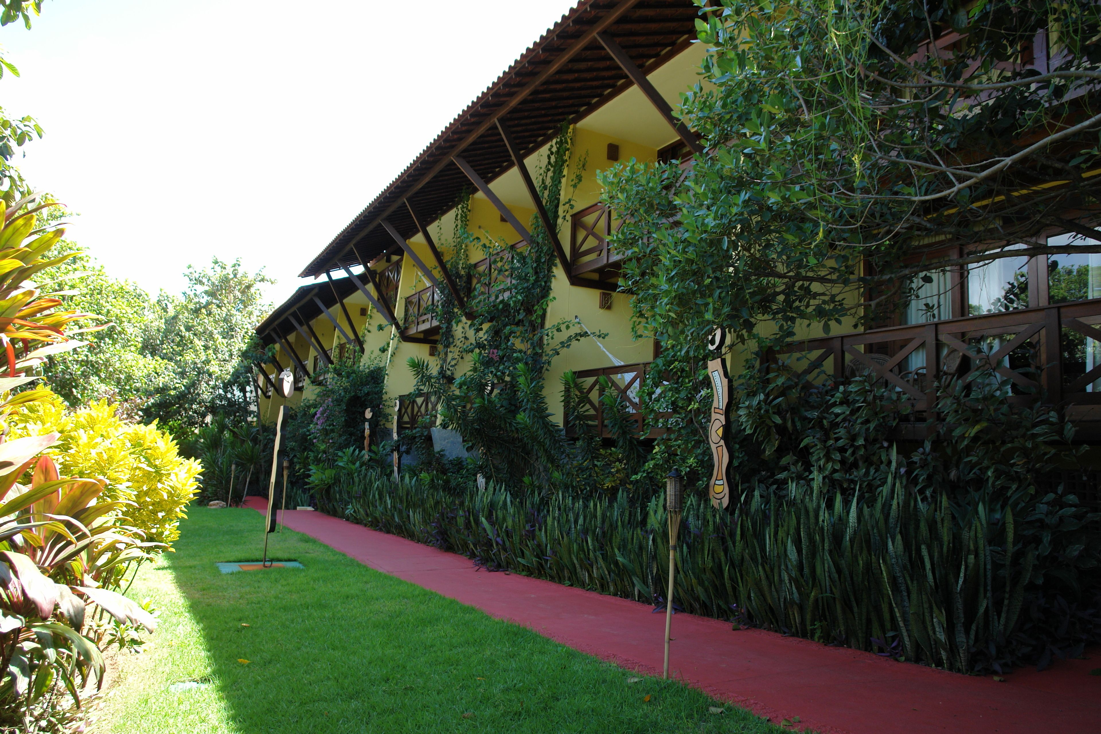 A building with a red pathway, surrounded by lush greenery and a yellow facade.