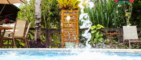 A pool area with a wooden planter of bananas, lounge chairs, and a sign for Pousada Thalassa Hotel.