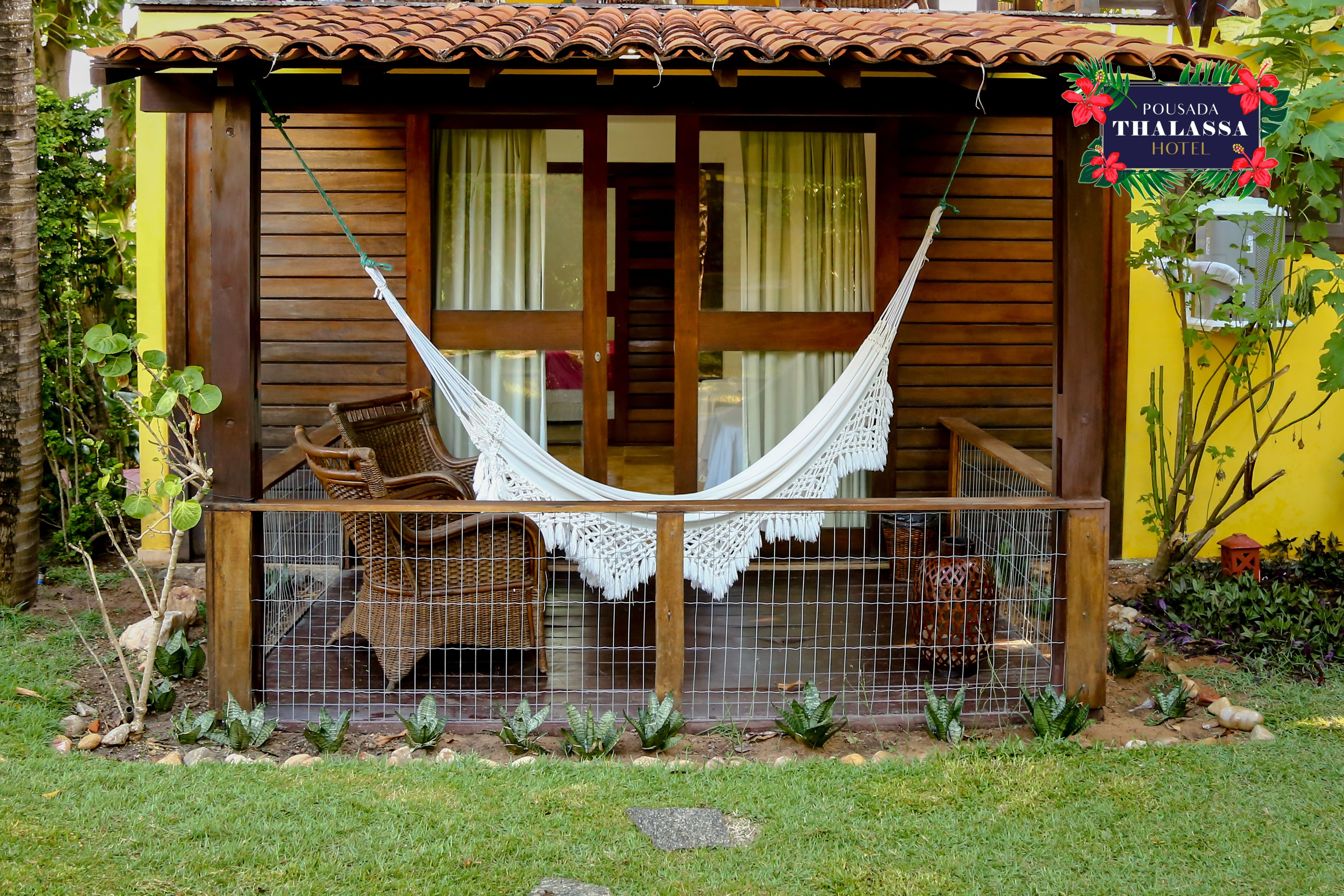 A wooden building with a hammock and wicker furniture outside.