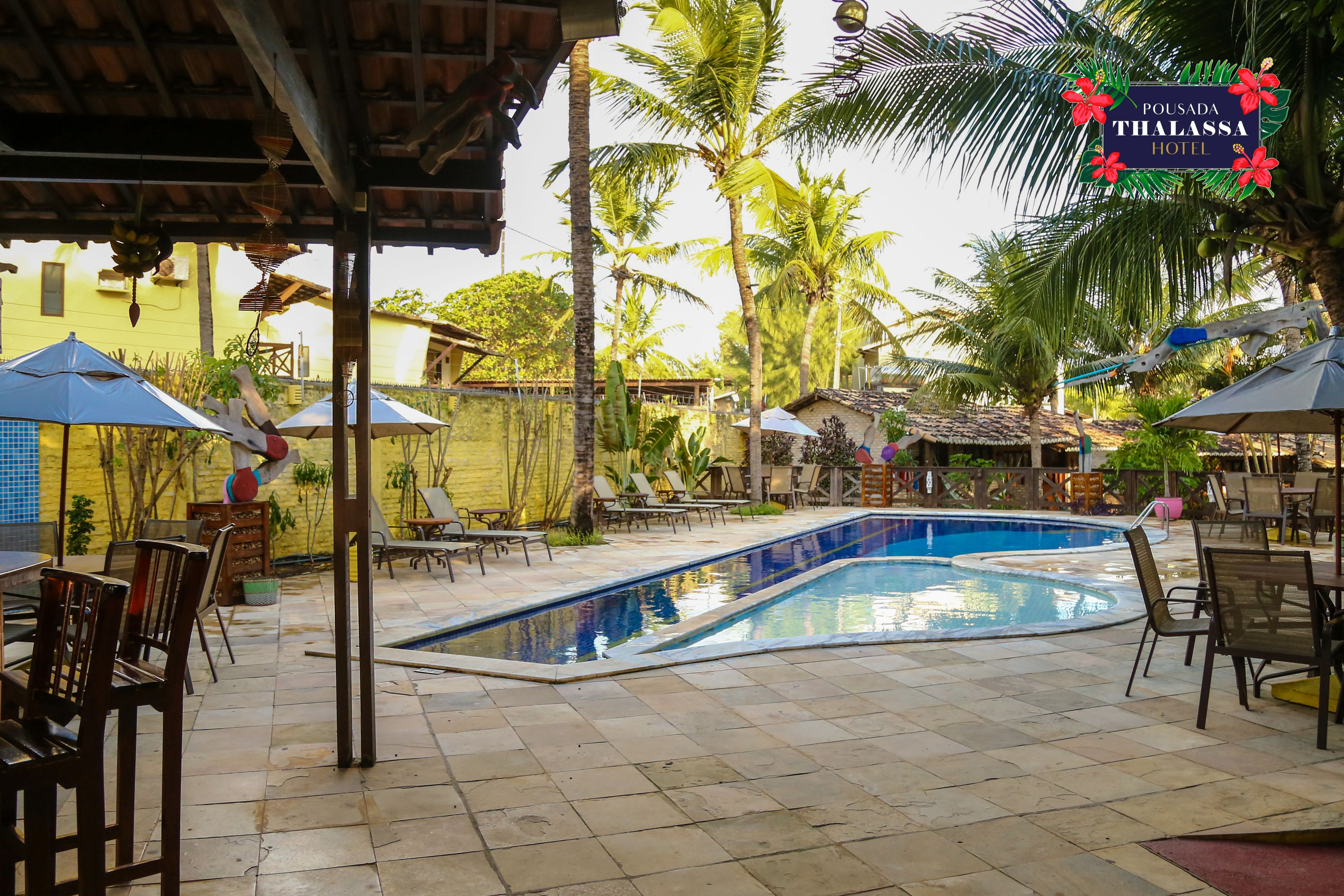 A pool area with lounge chairs and umbrellas, surrounded by palm trees and a yellow building.
