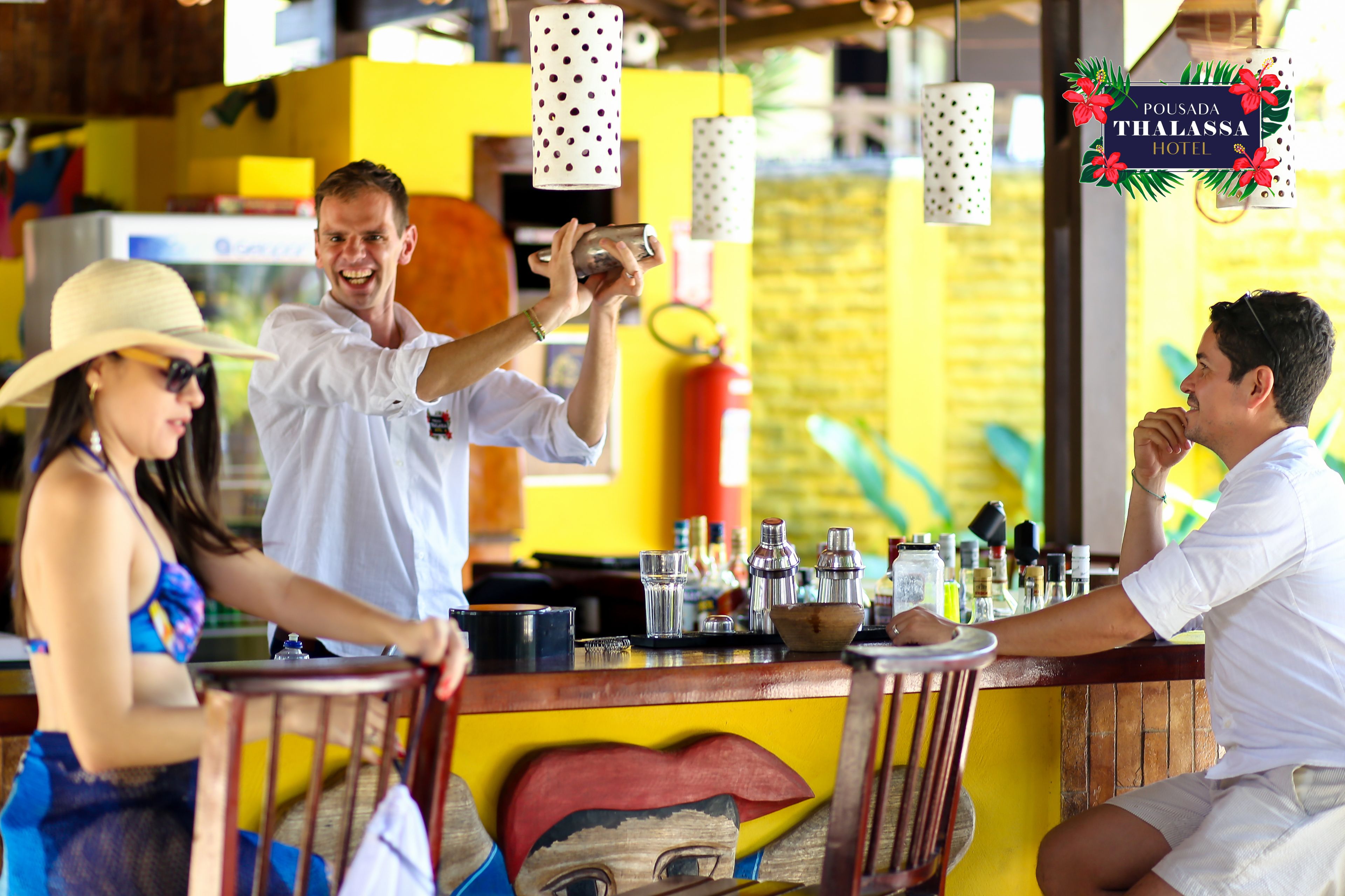 A bar area with a colorful mural, hanging lights, and a variety of bar tools and bottles.