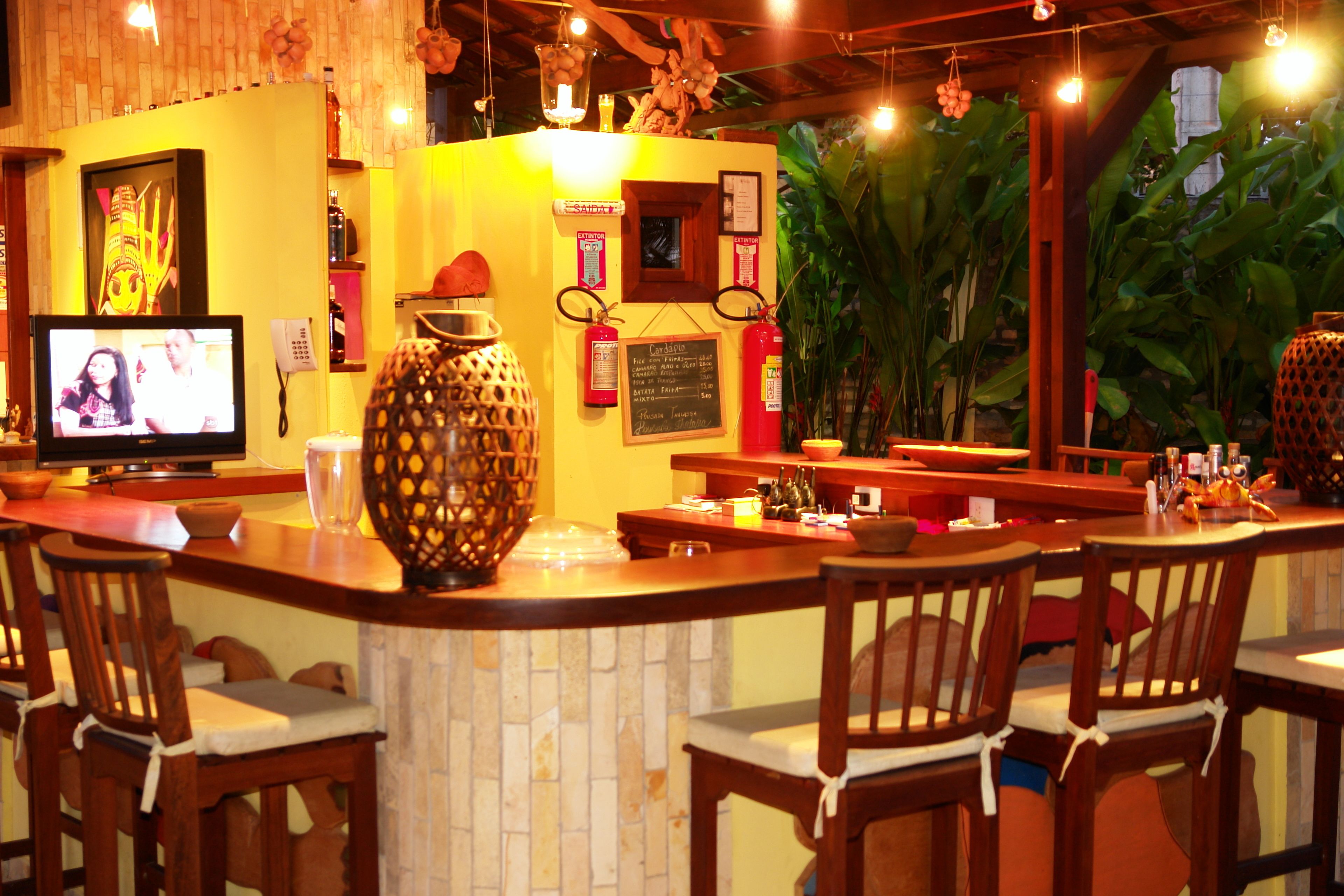 Un área de bar con sillas de madera, un televisor, un jarrón decorativo grande y una pizarra de menú.