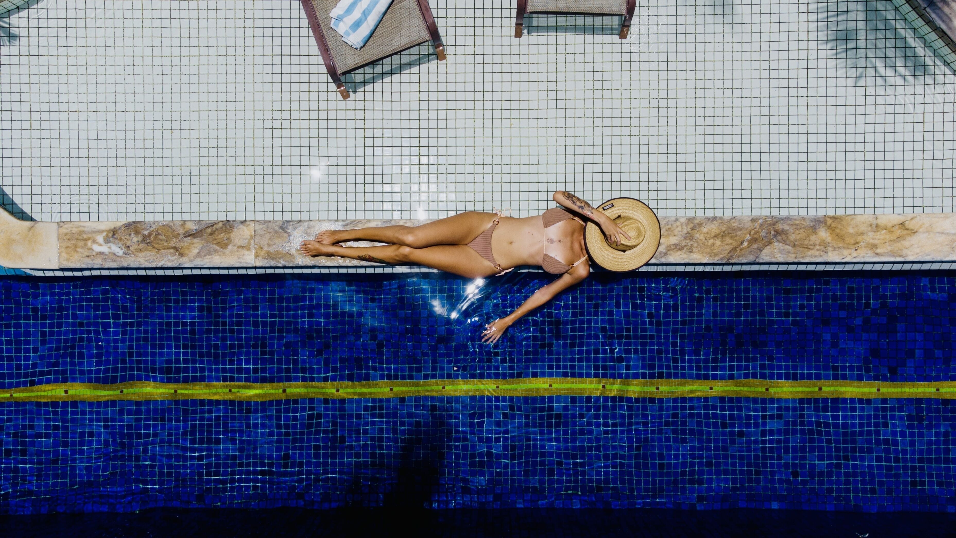 A person lying on a poolside lounge chair with a pool in the background.