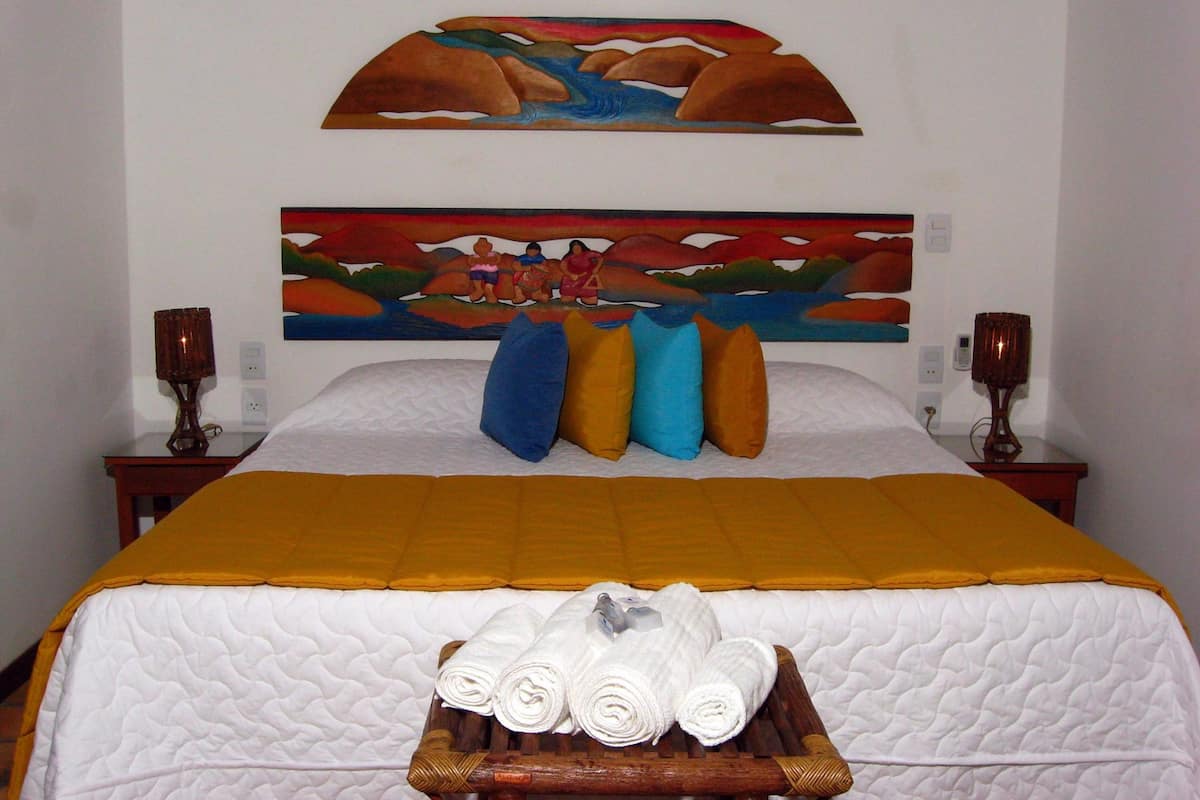 Une chambre d’hôtel avec un lit, un tableau au-dessus du lit, deux tables de chevet et un plateau avec des serviettes.