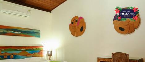 A hotel room with two beds, a small table, a wicker chair, and a wall painting.