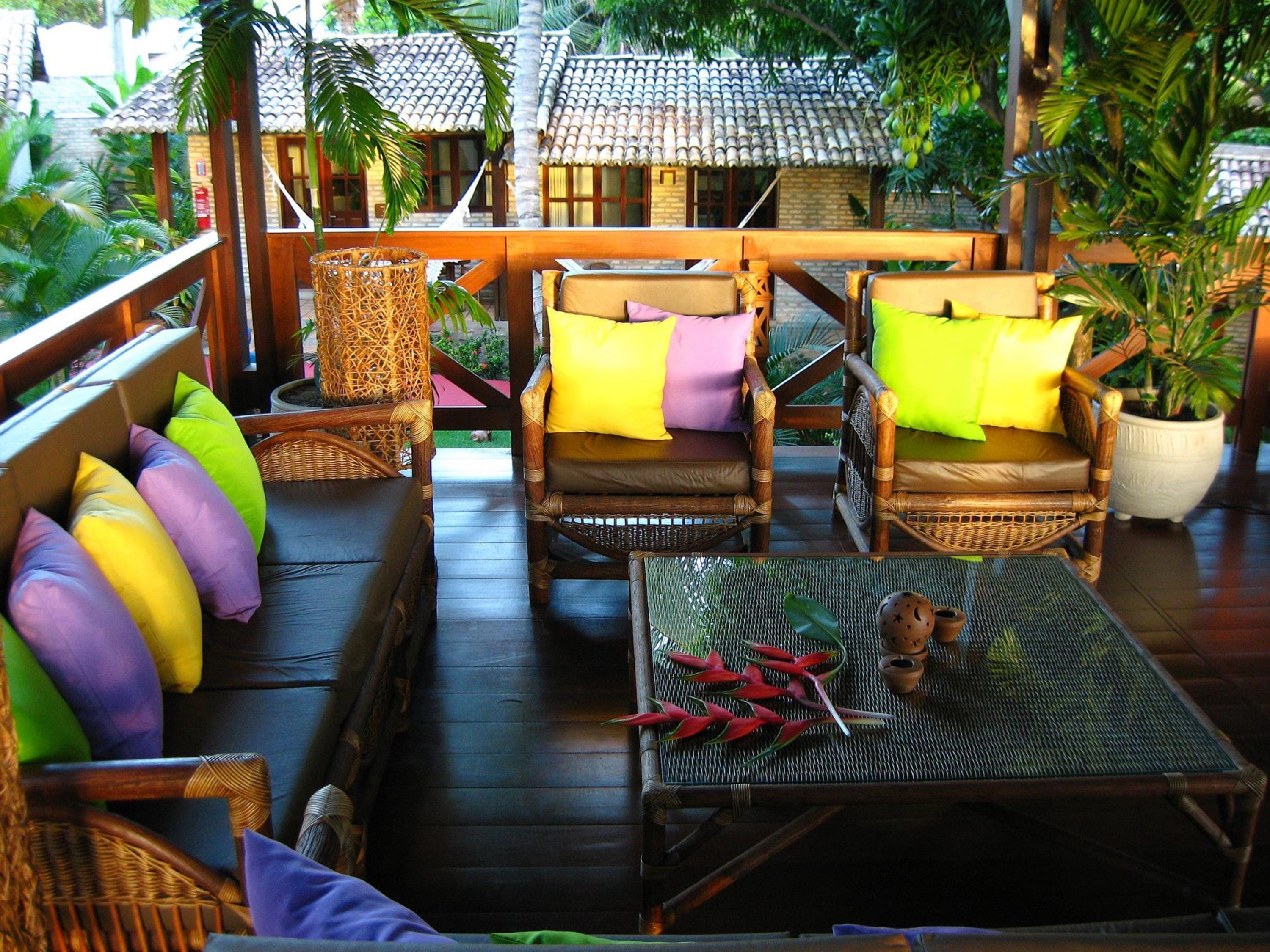 A wooden deck with wicker furniture, including two chairs and a bench with colorful cushions.