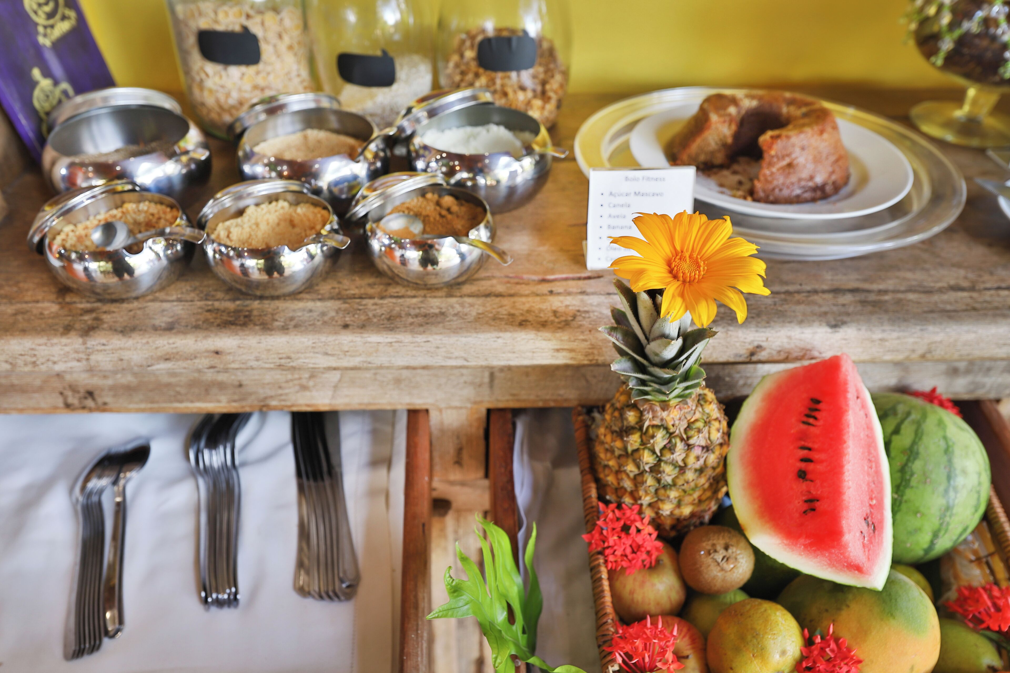 A wooden table with various food items, utensils, and a flower.