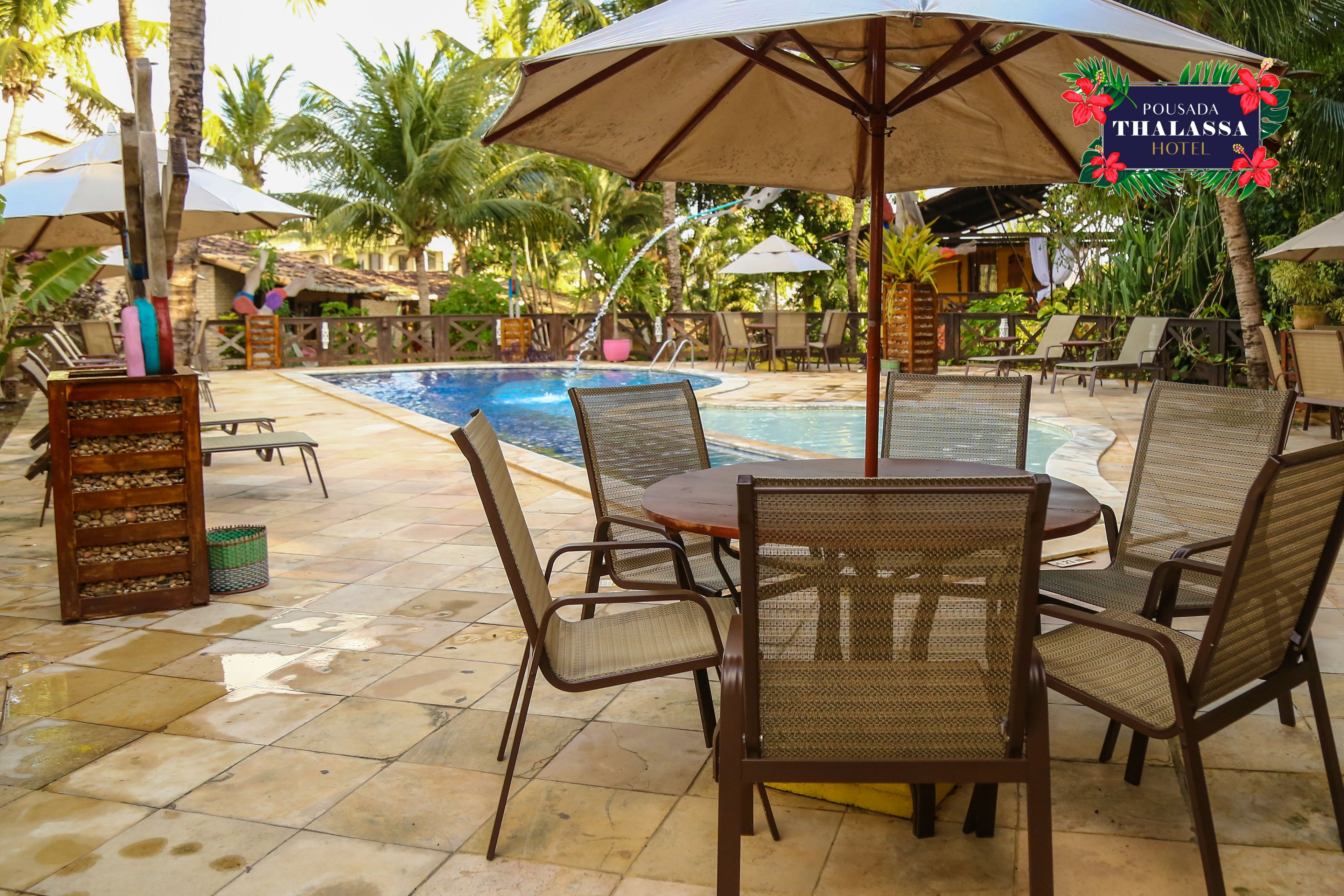 A poolside area with lounge chairs and umbrellas, a wooden chair with a basket, and a sign for Pousada Thalassa Hotel.