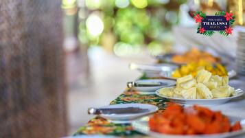 A buffet table with various dishes, including pineapple and red vegetables, at Pousada Thalassa Hotel.
