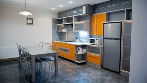 Eine moderne Küche mit grauen und orangefarbenen Schränken, einem Edelstahlkühlschrank und einem Essbereich mit Tisch und Stühlen.