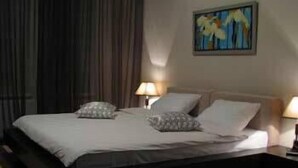 Ein ordentlich bezogenes Bett mit Kissen und Decke, zwei Nachttischlampen und ein Gemälde an der Wand.
