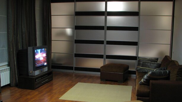 Ein modernes Wohnzimmer mit Flachbildfernseher, einem braunen Sofa, einem passenden Hocker und einer großen Schiebeglastür mit Blick.