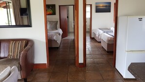 Habitación de hotel con cama, una mesita, refrigerador y baño a la vista a través de una puerta abierta.